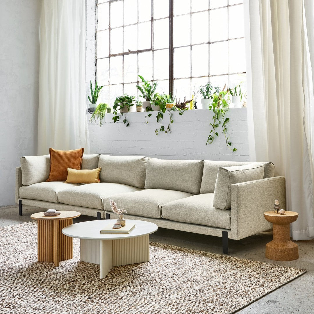 Light beige sofa with textured tan and mustard pillows, paired with natural wood and white accent tables, and a woven rug.