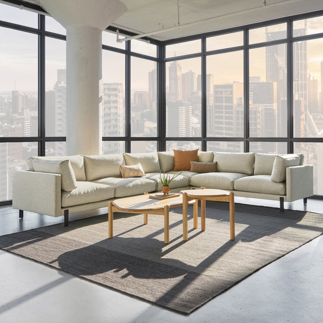 Light beige sectional sofa with warm orange cushions, set on a gray rug in a modern urban environment.