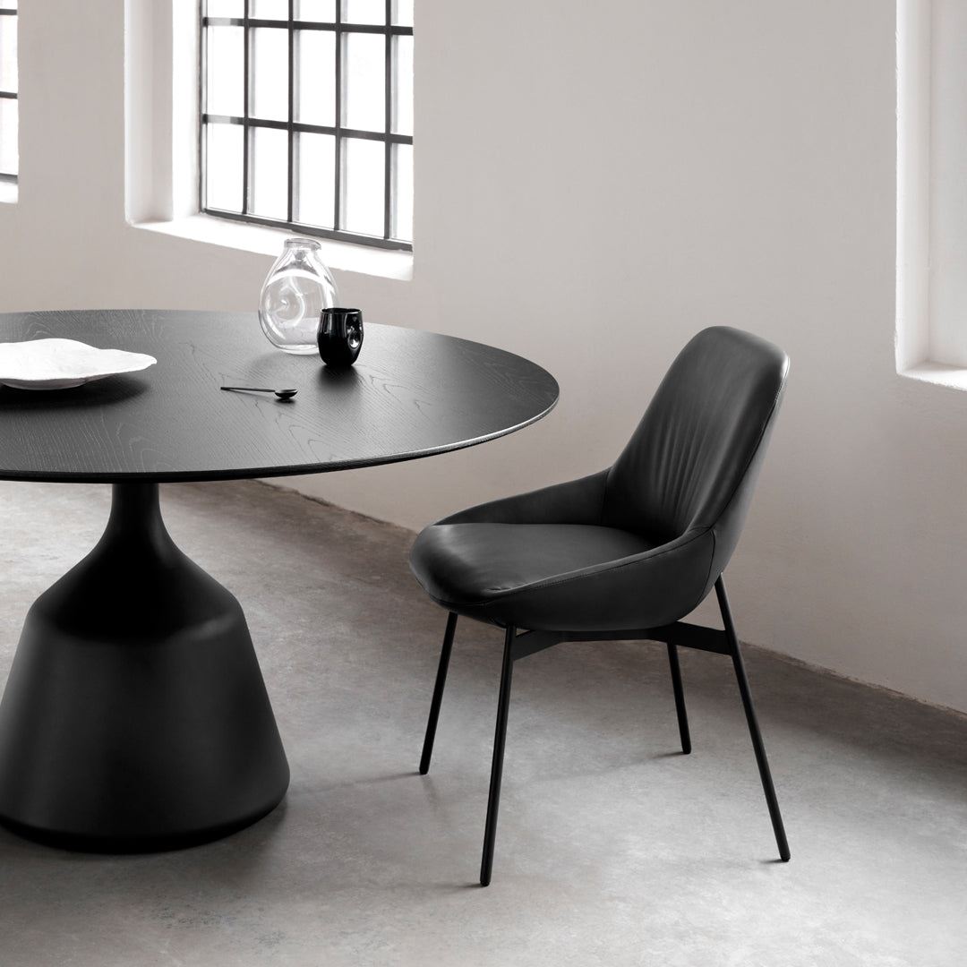 Black round table and sleek black chair set against a light gray floor and minimalistic white walls.