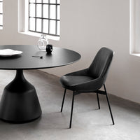 Black round table and sleek black chair set against a light gray floor and minimalistic white walls.