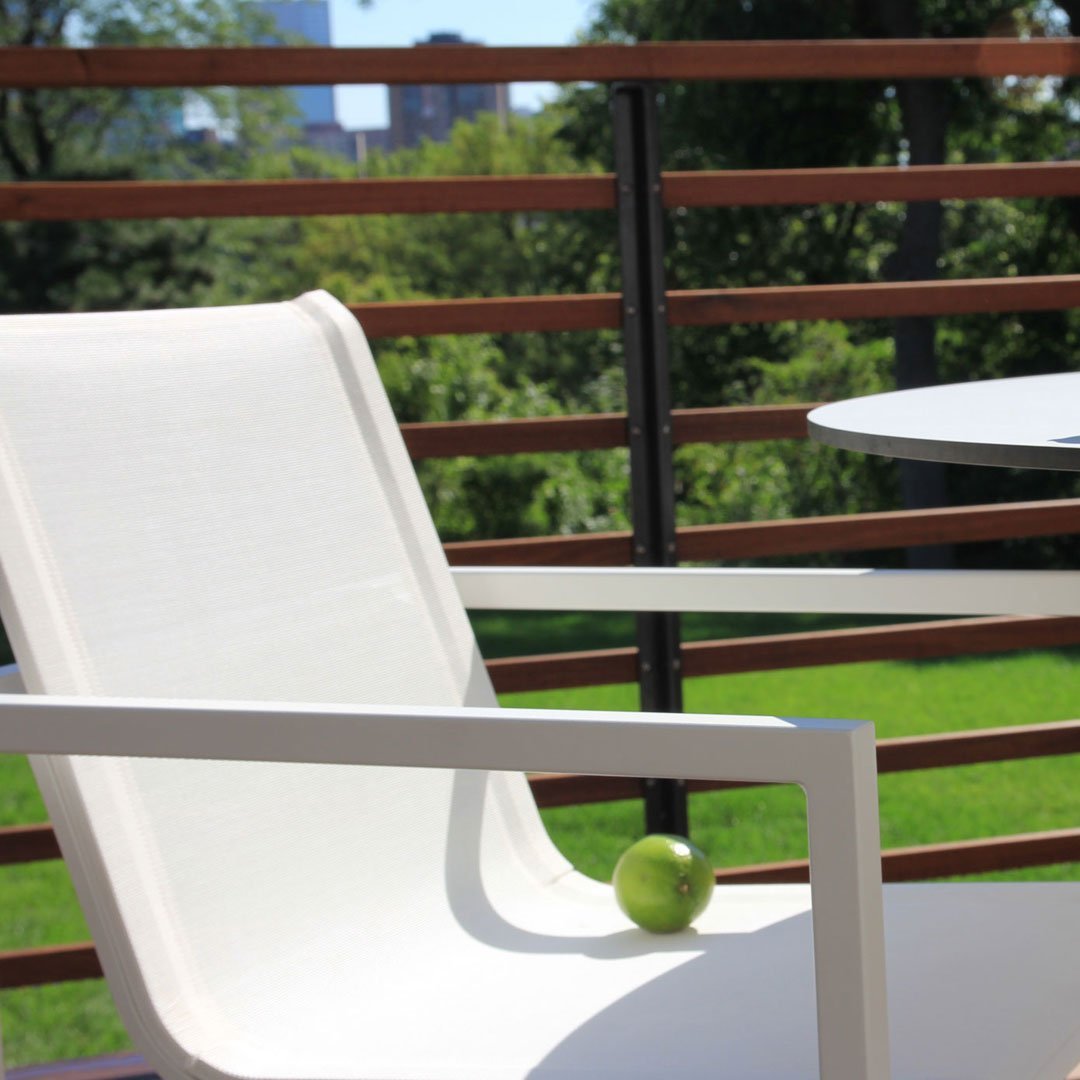 White patio chair with a smooth fabric design, set against a lush green background and sleek wooden railing.