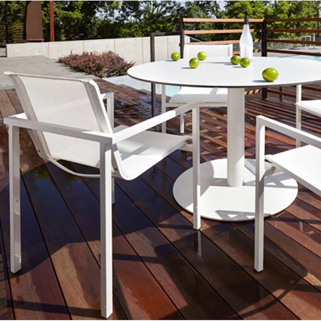 White outdoor dining set with minimalist design on a wooden deck, featuring green accents from limes.