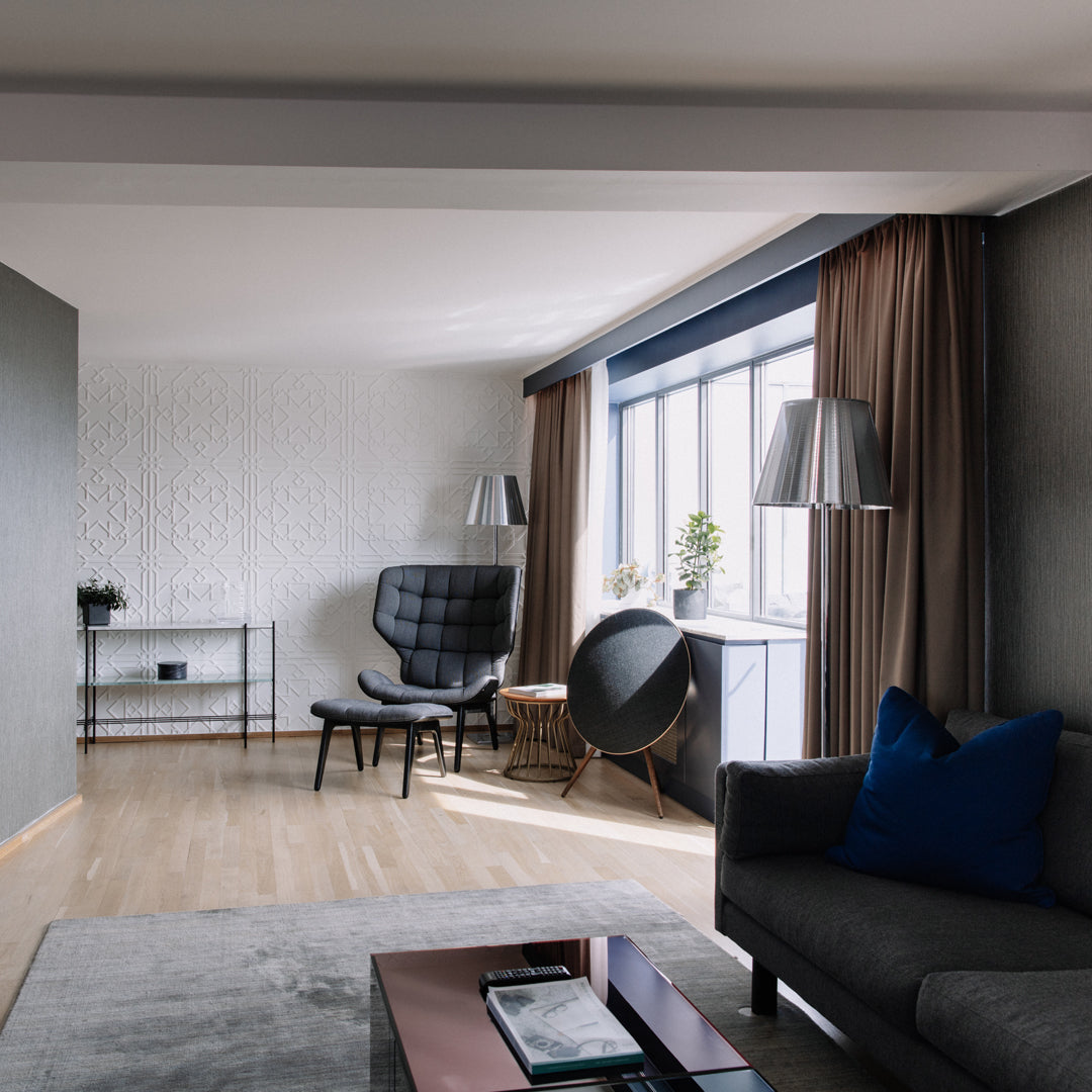 Contemporary living room featuring beige walls, grey furniture, blue accents, and light wood flooring. Elegant patterns throughout.