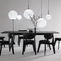 Modern black dining table with sleek chairs, accented by round, white pendant lights against a neutral gray backdrop.