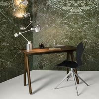 Modern wooden desk with tapered legs, black chair, and metallic accents against a textured green patterned wall.