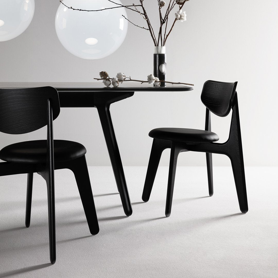 Black dining table and chairs with sleek, modern lines against a light gray backdrop, featuring minimalist design elements.