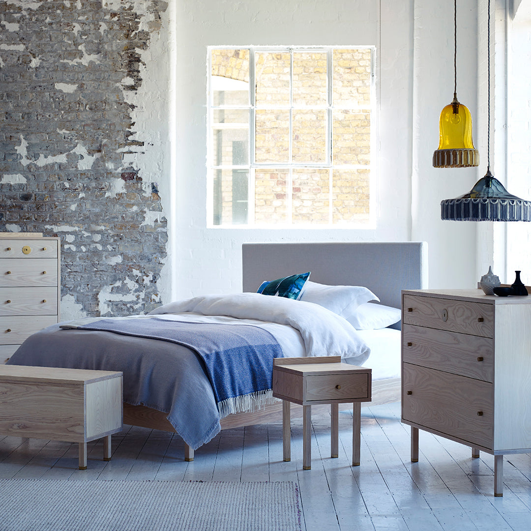 Modern bedroom with gray and white bedding, natural wood furniture, and colorful pendant lights in a bright, minimalist space.