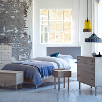 Modern bedroom with gray and white bedding, natural wood furniture, and colorful pendant lights in a bright, minimalist space.