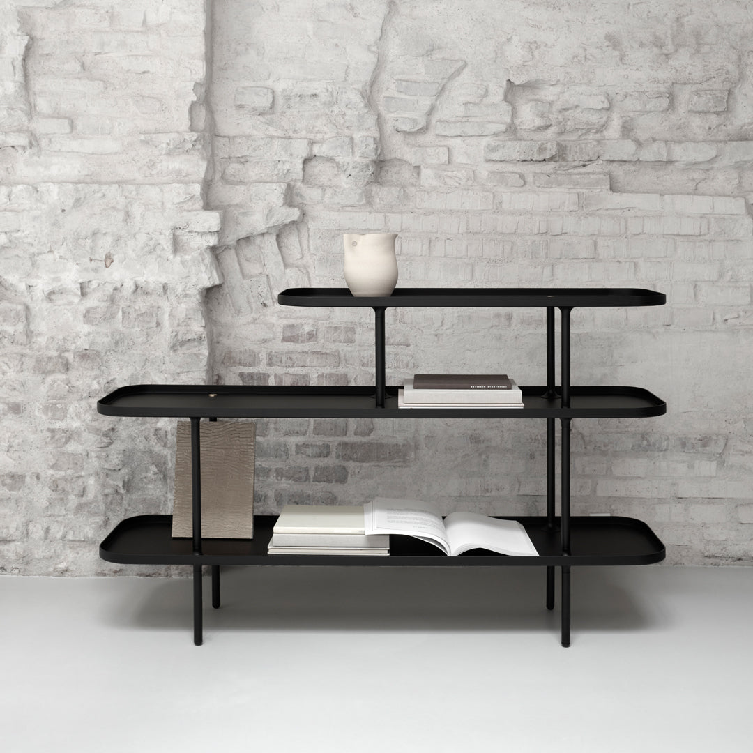 Sleek black shelf with minimalist design, set against a textured gray brick wall.