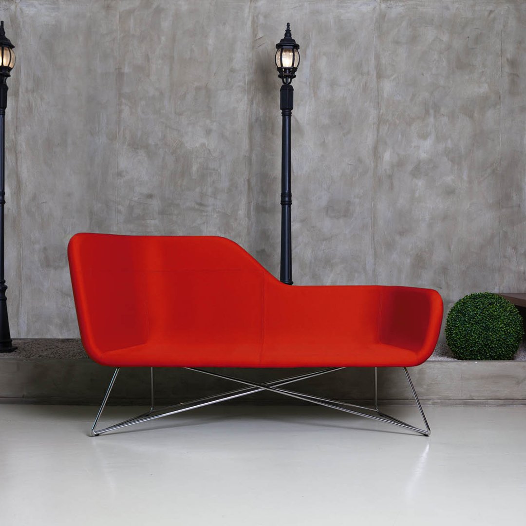 Modern red sofa with a sleek curved design and stainless steel legs, set against a textured gray background.