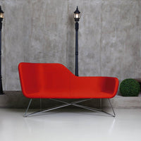 Modern red sofa with a sleek curved design and stainless steel legs, set against a textured gray background.
