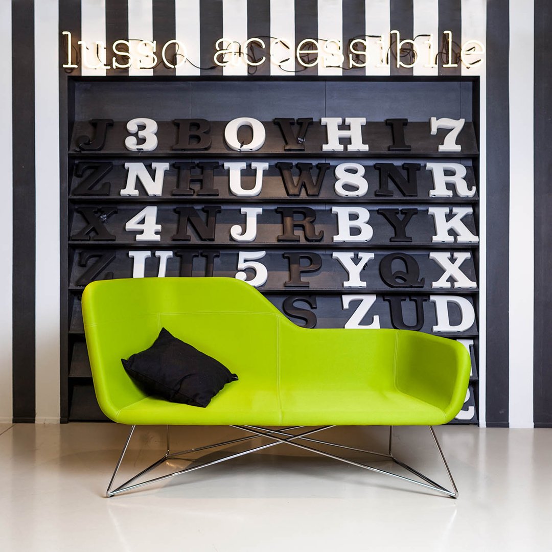 Bright green modern couch with a black accent pillow against bold black and white striped backdrop.