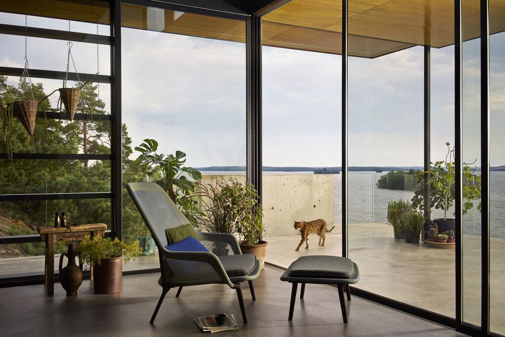 Modern lounge chair in green with a blue accent pillow, surrounded by greenery and natural wood tones, bright and airy setting.