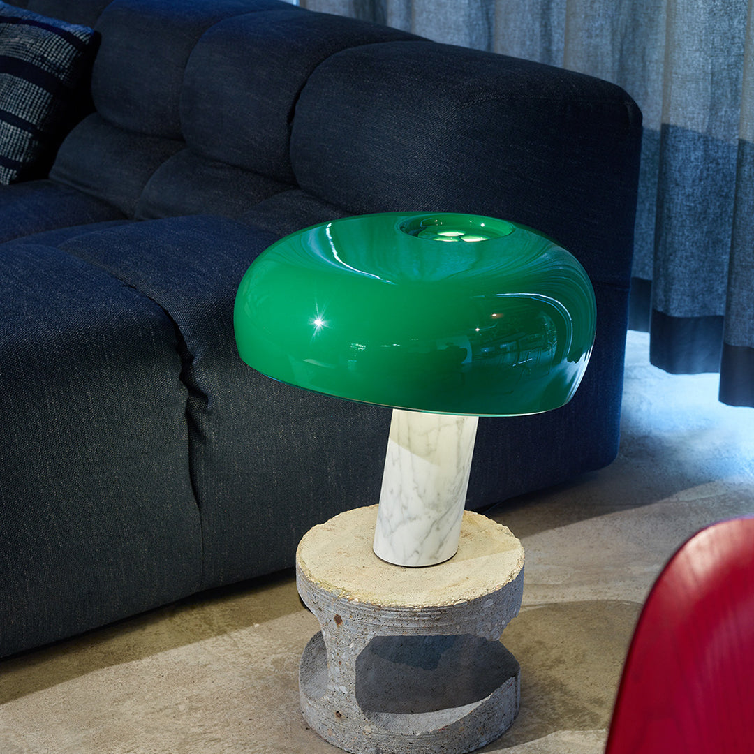 Green mushroom-shaped lamp with a glossy finish on a marble base, set against a textured dark sofa and soft neutral floor.