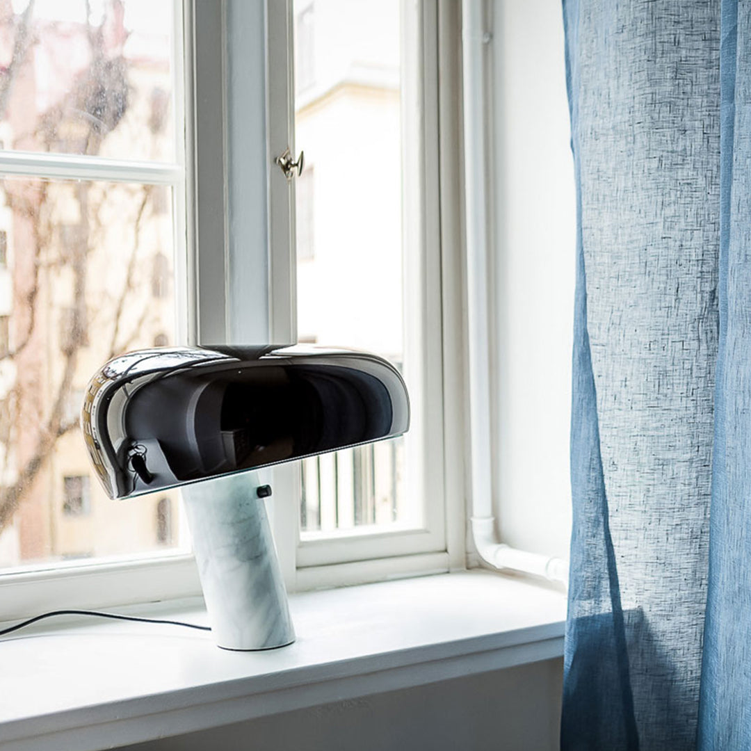 Glossy black lamp with a marble base, set against a backdrop of light grey curtains and natural light.