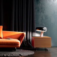 Orange retro sofa, black textured curtains, sleek black lamp, and wooden nightstand on dark wood flooring.