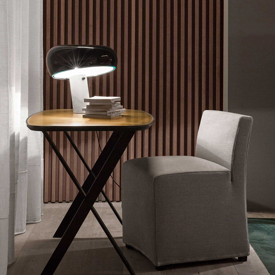 Stylish black lamp on a wooden table beside a light gray chair against a backdrop of dark wooden slats.