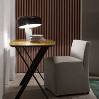 Stylish black lamp on a wooden table beside a light gray chair against a backdrop of dark wooden slats.