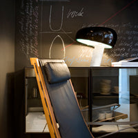 "Stylish black and wood lounge chair against a dark, textured wall with white chalk patterns and a sleek lamp."