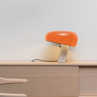 Orange dome lamp with a marble base, featuring a sleek, modern design against a light wall for a stylish aesthetic.