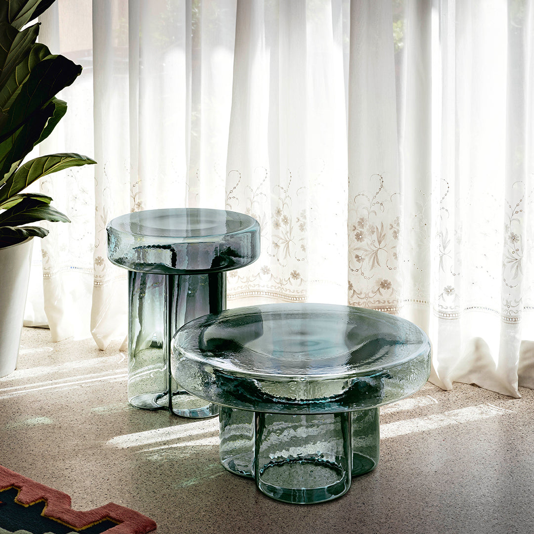 Clear glass side tables with a unique, layered round and cylindrical design, reflecting light and creating soft shadows.