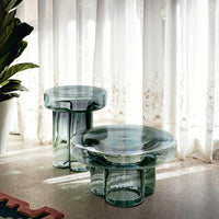 Clear glass side tables with a unique, layered round and cylindrical design, reflecting light and creating soft shadows.
