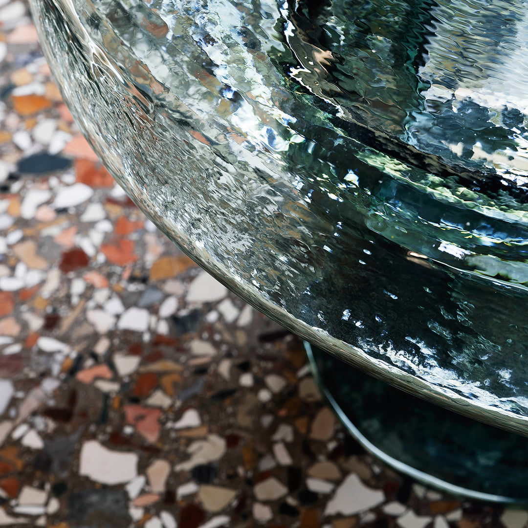 Clear turquoise glass bowl reflecting colorful speckled terrazzo pattern underneath. Modern and stylish design.
