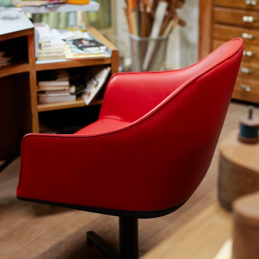 Red curved chair with smooth, modern design and black base, set against a warm wooden background.