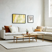 Cozy white sofa with orange, cream, and earthy tones; features abstract wall art and textured neutral rug.