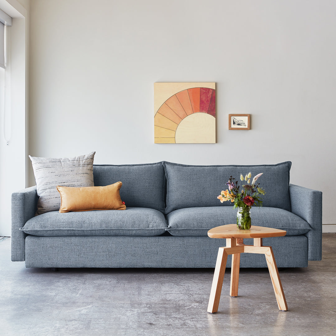 Gray fabric sofa with orange and beige accent pillows, paired with a light wood side table, in a neutral-toned setting.