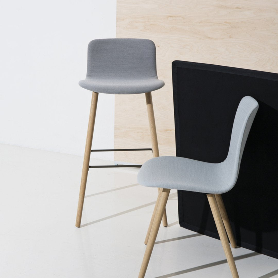 Two modern gray bar stools with wooden legs, minimalist design against a simple black and light wood backdrop.