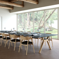 Modern workspace featuring a dark gray table, light wood chairs with black seats, and natural light through large windows.