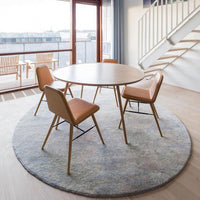 Circular light blue rug with intricate patterns beneath a round wooden table and orange-accented chairs.