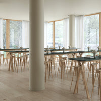 "Modern dining space with light wood floors, natural light, white curtains, and minimalist black tabletops."