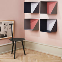 Colorful wall-mounted storage boxes in navy, rose, and white against a soft pink wall. Black wooden chair in foreground.