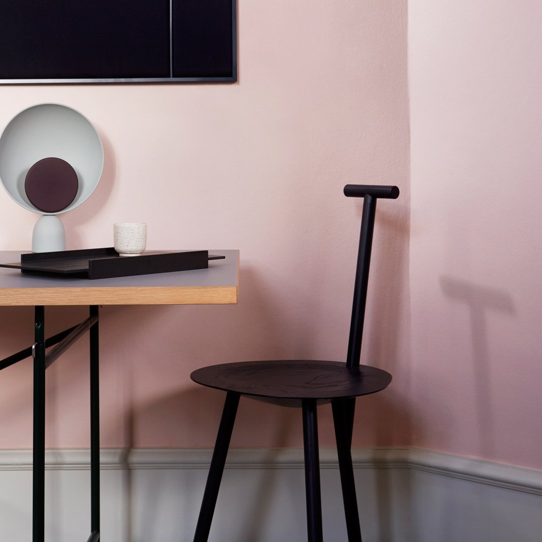 Stylish black chair and modern desk against soft pink walls, featuring minimalistic shapes and neutral decor accents.