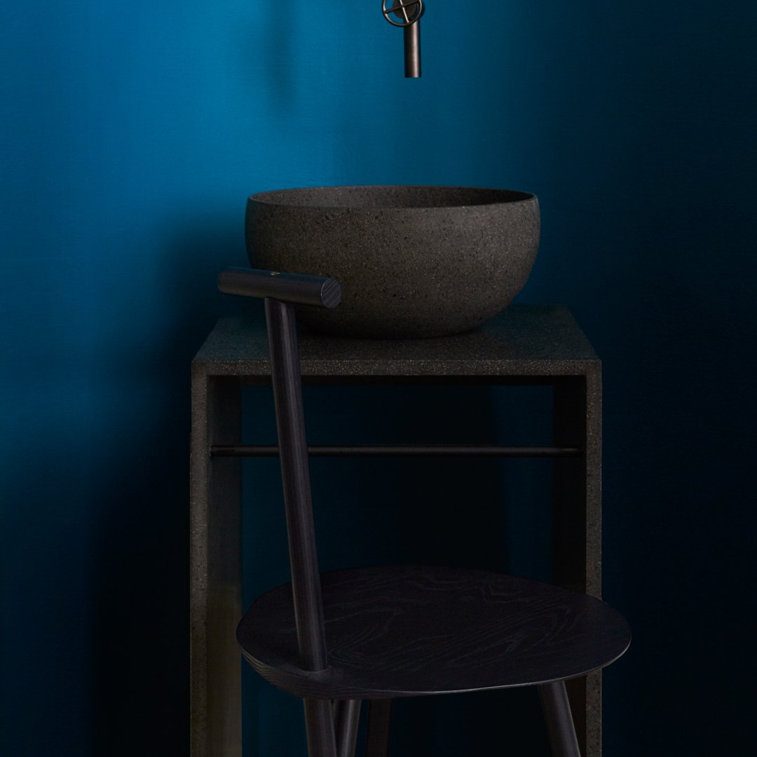 Black bowl on a dark gray table with a sleek black chair against a vibrant blue background. Modern minimalist design.