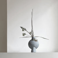 Grey textured vase with minimalist design, featuring simple green stems against a neutral background.