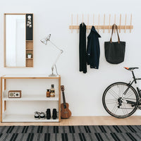 Modern entryway scene featuring a striped black and grey rug, complemented by wooden accents and neutral colors.