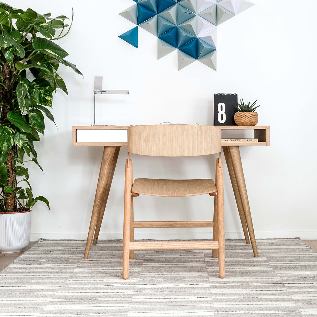 Light wood desk and chair with a neutral rug; geometric teal and blue wall art adds a modern touch.