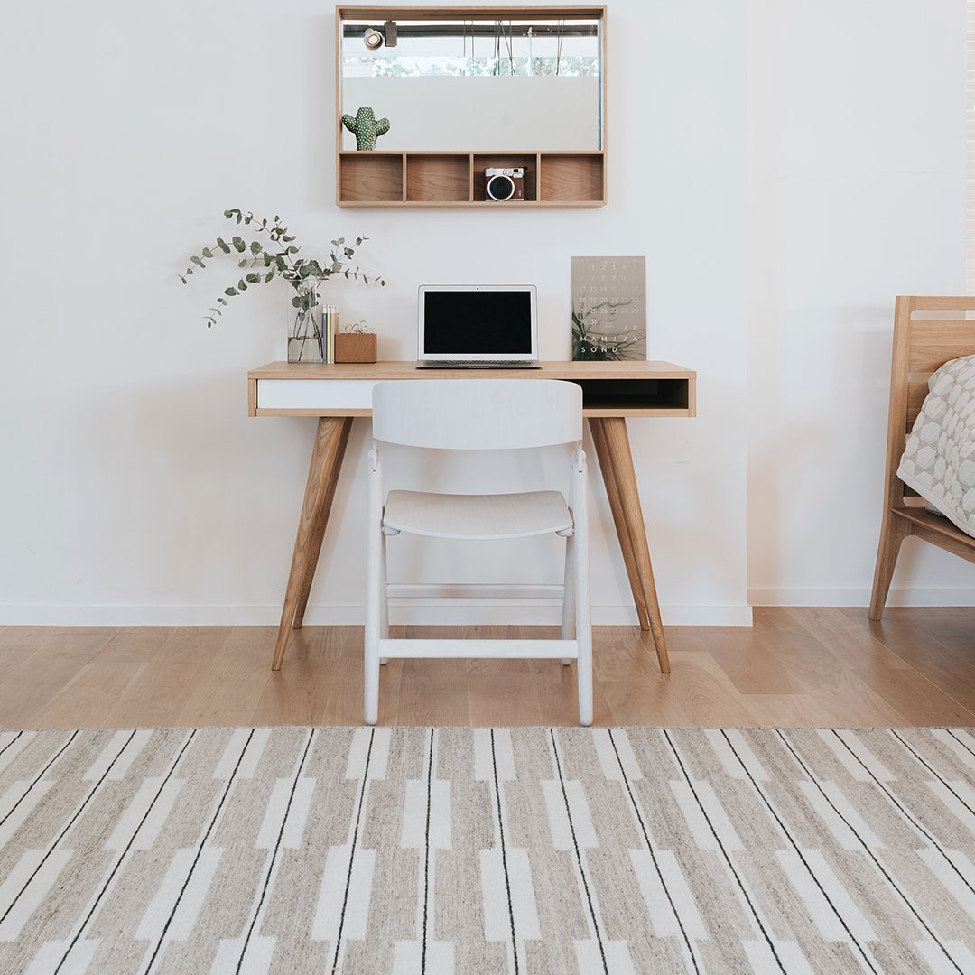 Neutral-toned rug with a striped pattern in shades of beige and gray, enhancing a minimalist workspace aesthetic.