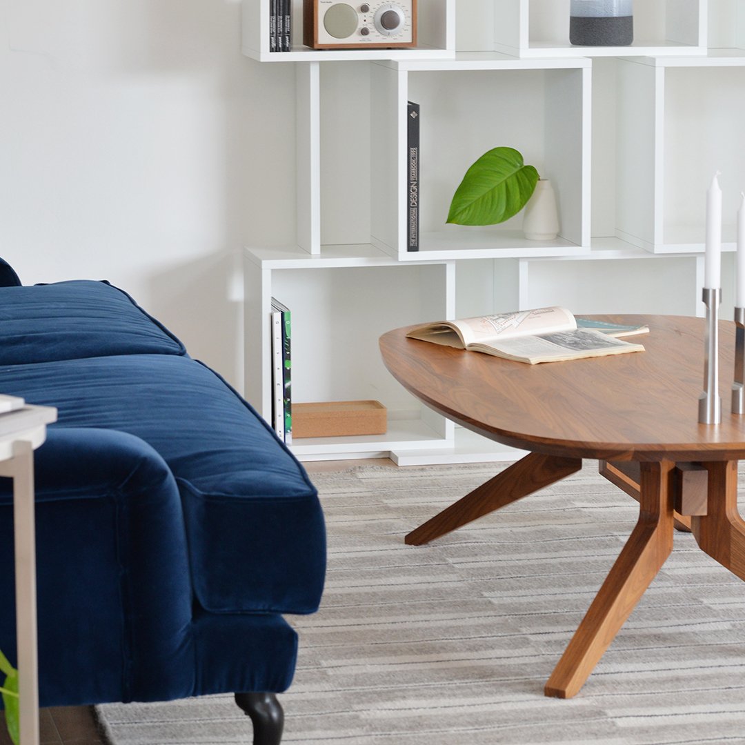 "Plush navy blue sofa with a modern wooden coffee table and neutral patterned rug in a bright, minimalist living space."
