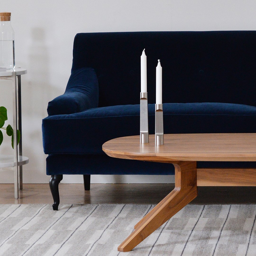 Navy velvet sofa and wooden coffee table with a light striped rug, complemented by modern silver candle holders.