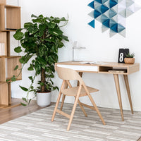 Contemporary desk in natural wood tones, paired with a light chair, accented by geometric blue wall art and a patterned rug.