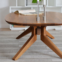 Round wooden coffee table with a rich walnut finish and contrasting light wood legs, set on a textured gray rug.