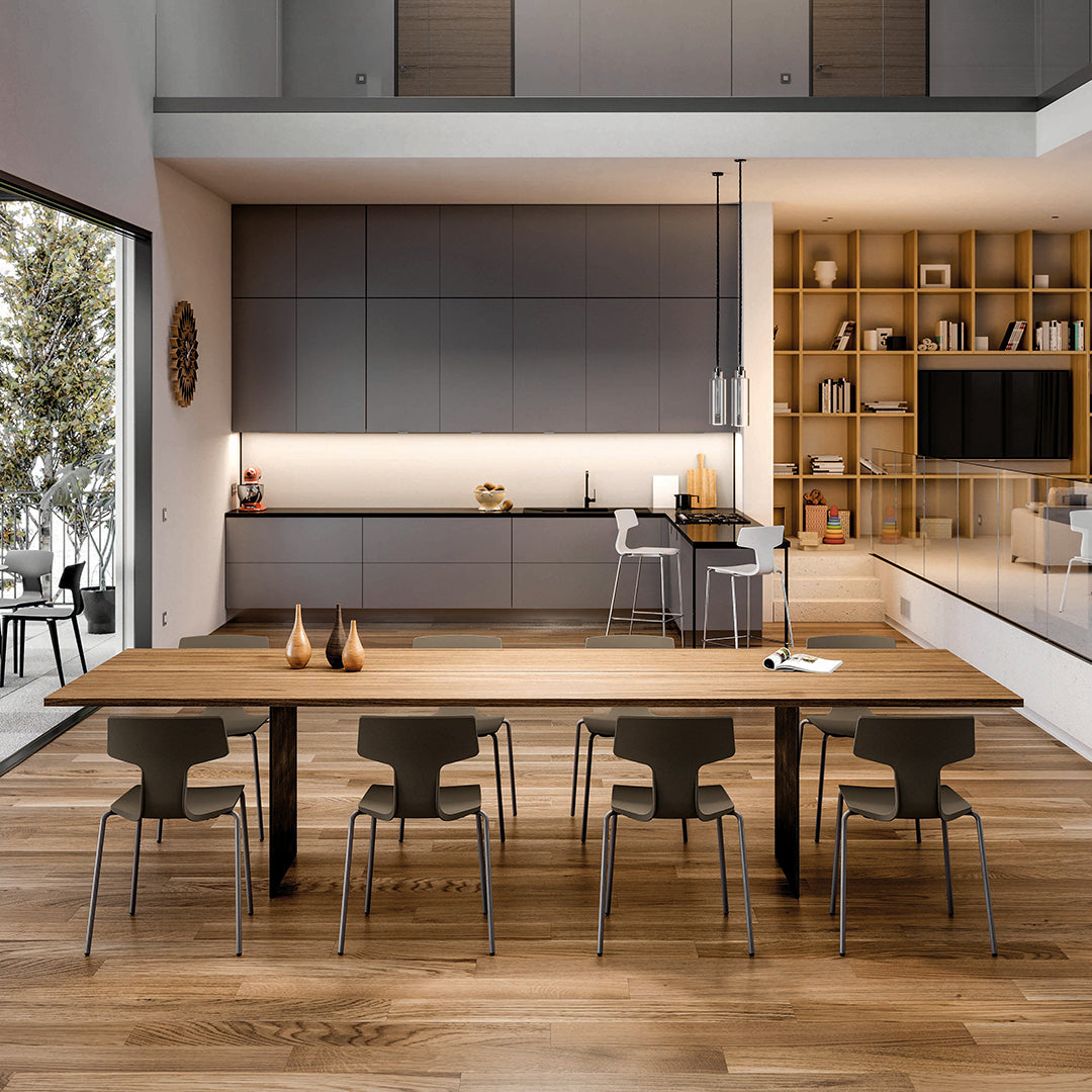 Contemporary kitchen with gray cabinets, wooden dining table, and sleek black and gray chairs on warm wooden flooring.