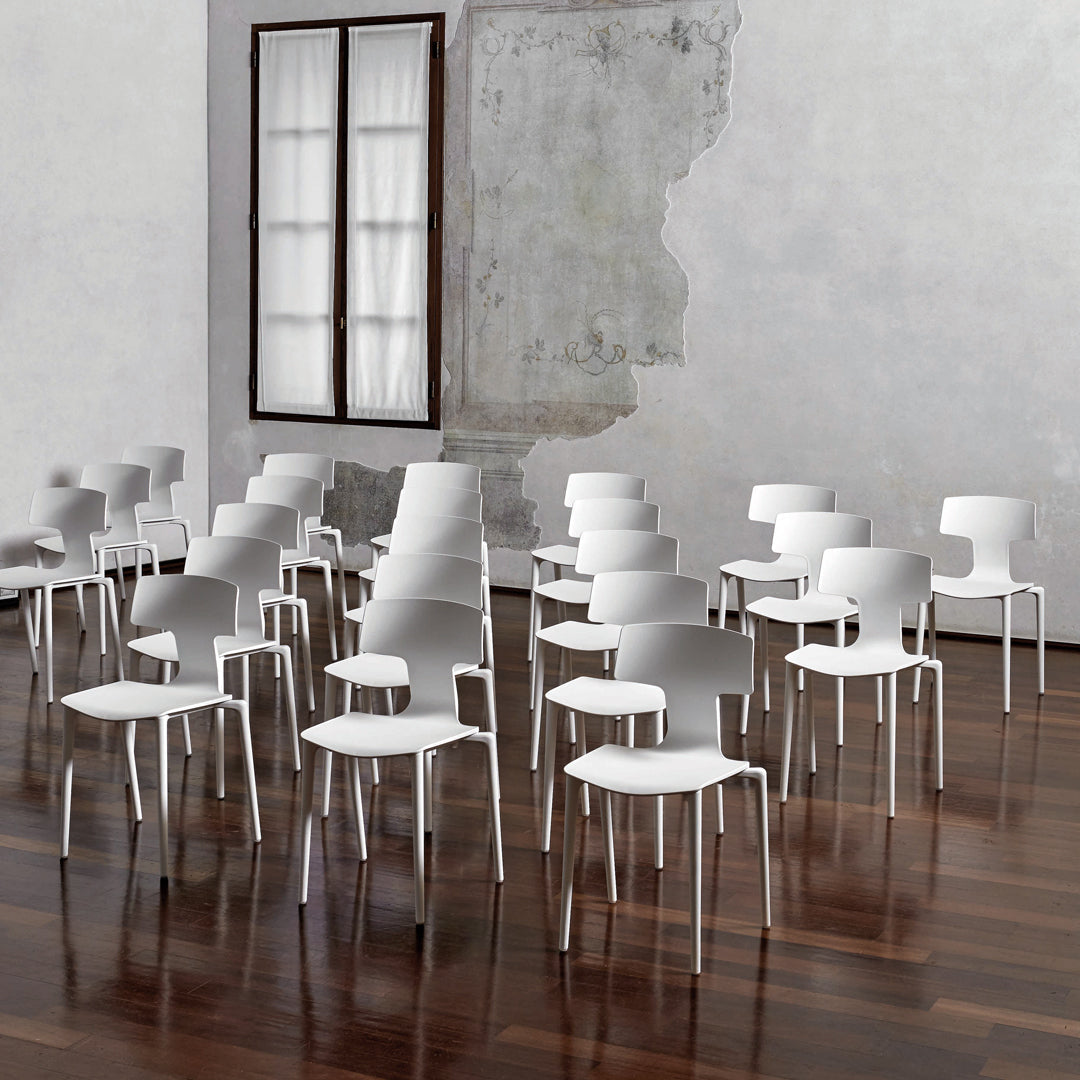 White minimalist chairs arranged on a polished wooden floor, set against a textured gray wall and natural light from a window.