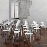 White minimalist chairs arranged on a polished wooden floor, set against a textured gray wall and natural light from a window.