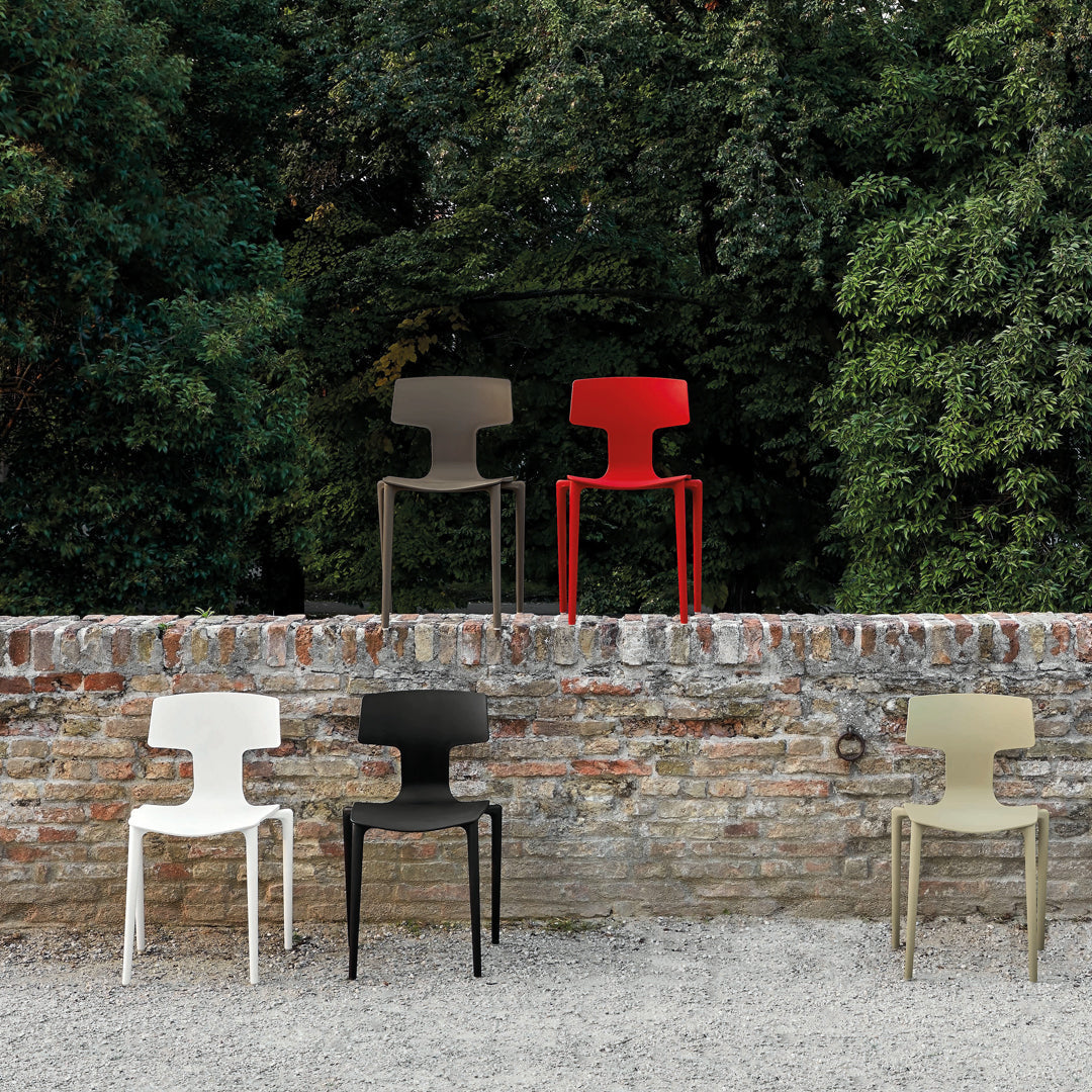 Vibrant modern chairs in red, cream, black, brown, and olive green against a rustic stone wall backdrop.