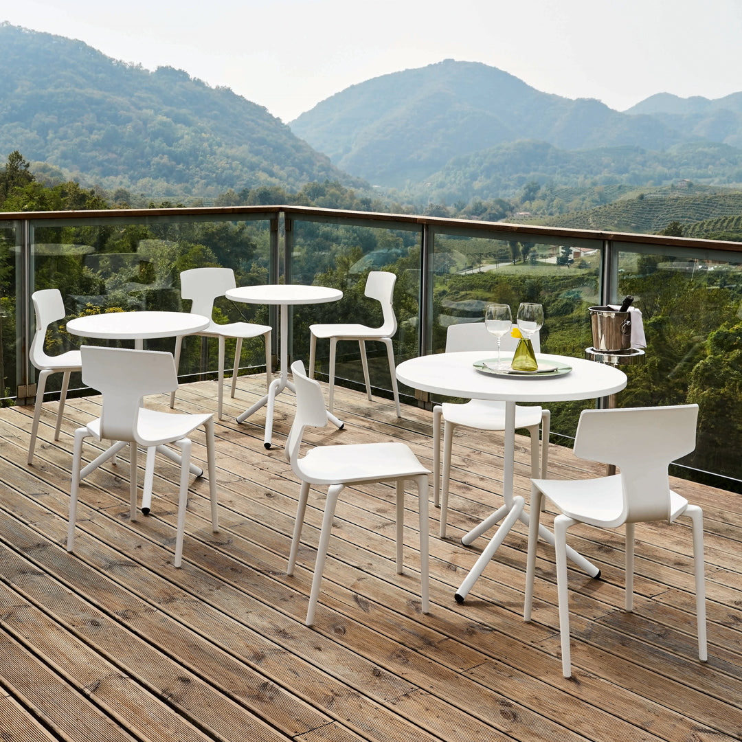 White outdoor dining set featuring sleek, modern design against a natural wood deck and scenic mountain backdrop.